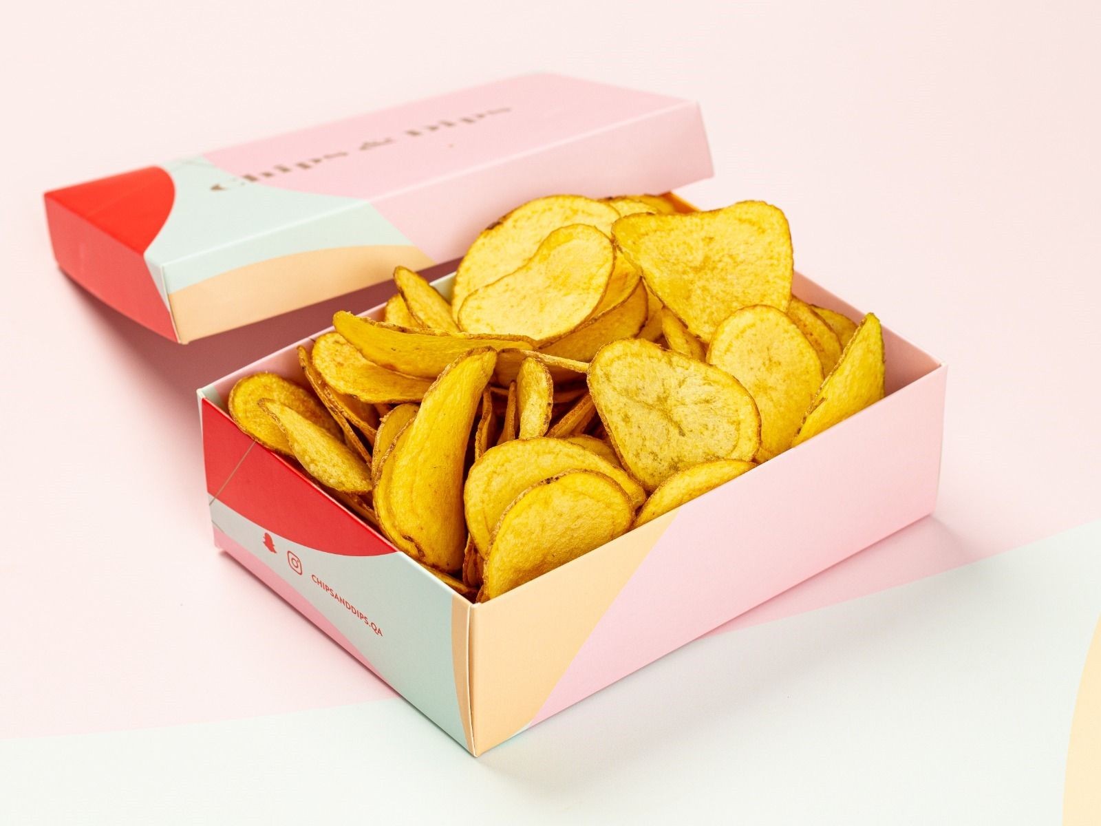 Open pink box filled with golden potato chips on a light pink background.