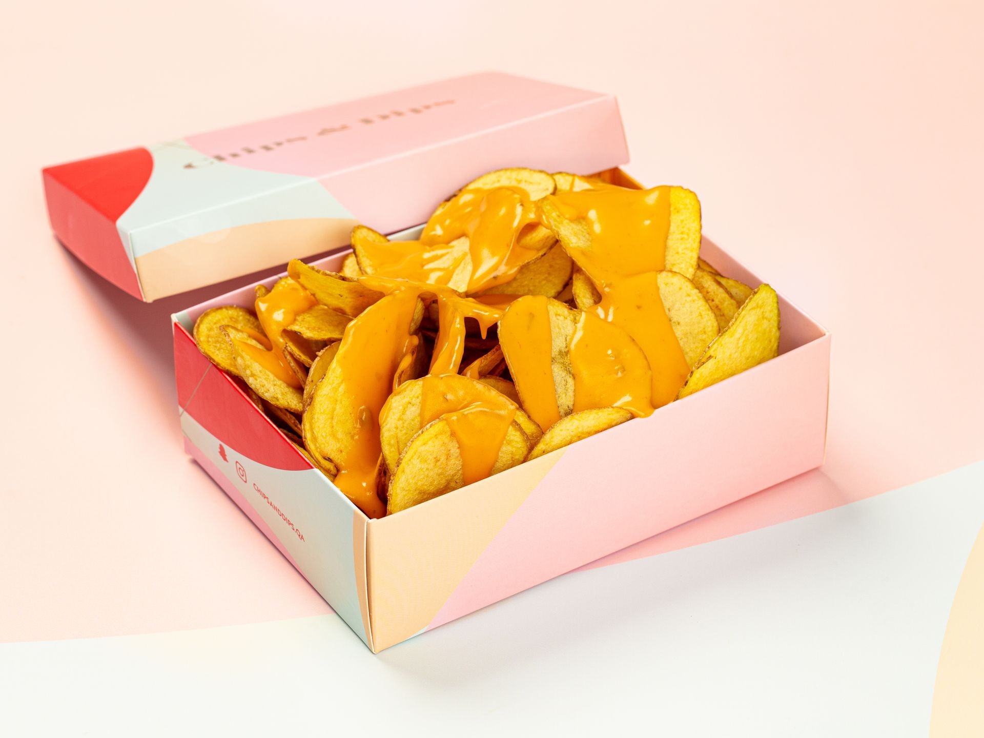 Box of potato chips topped with melted cheese sauce, placed on a pastel-colored background.